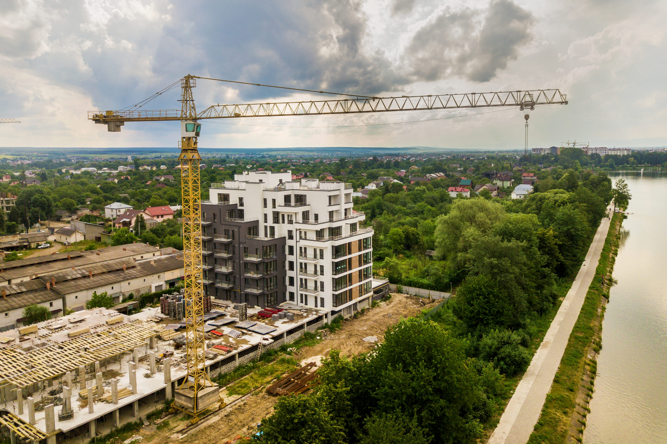 FerkoMedia - Aerial view of tower lifting crane and concrete frame of tall apartment residential building under construction in a city. Urban development and real estate growth concept.